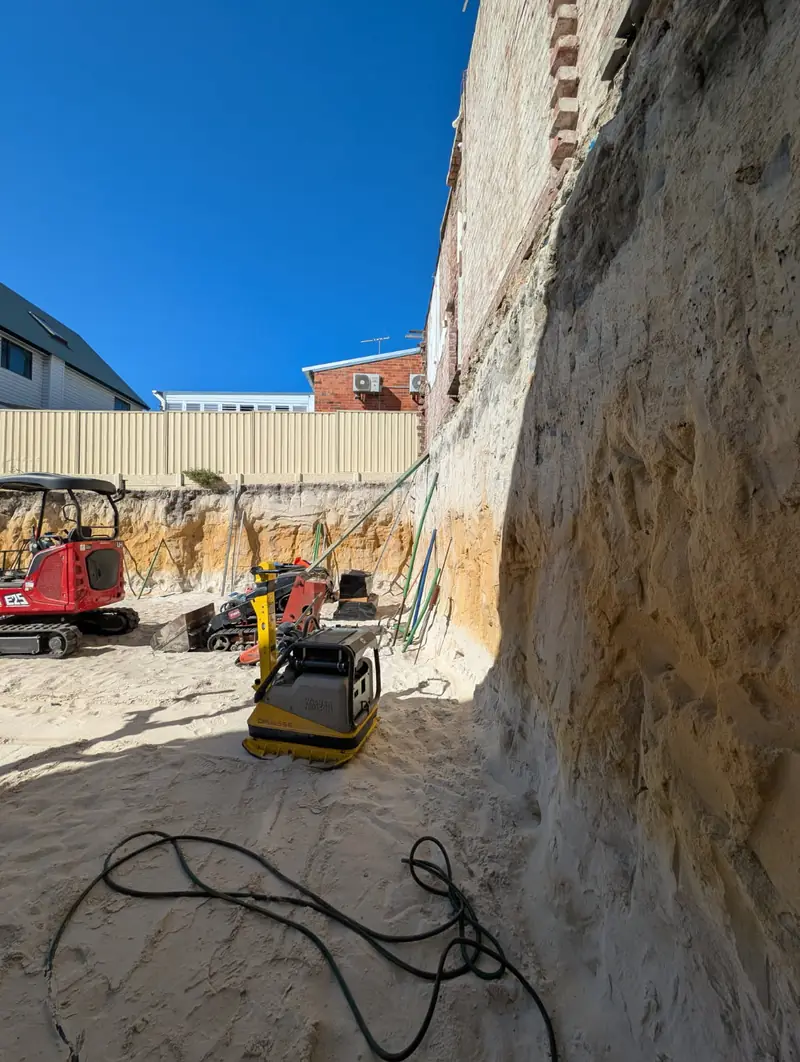 Deep excavation with a tall stabilised sand face, a mini excavator and plate compactor below